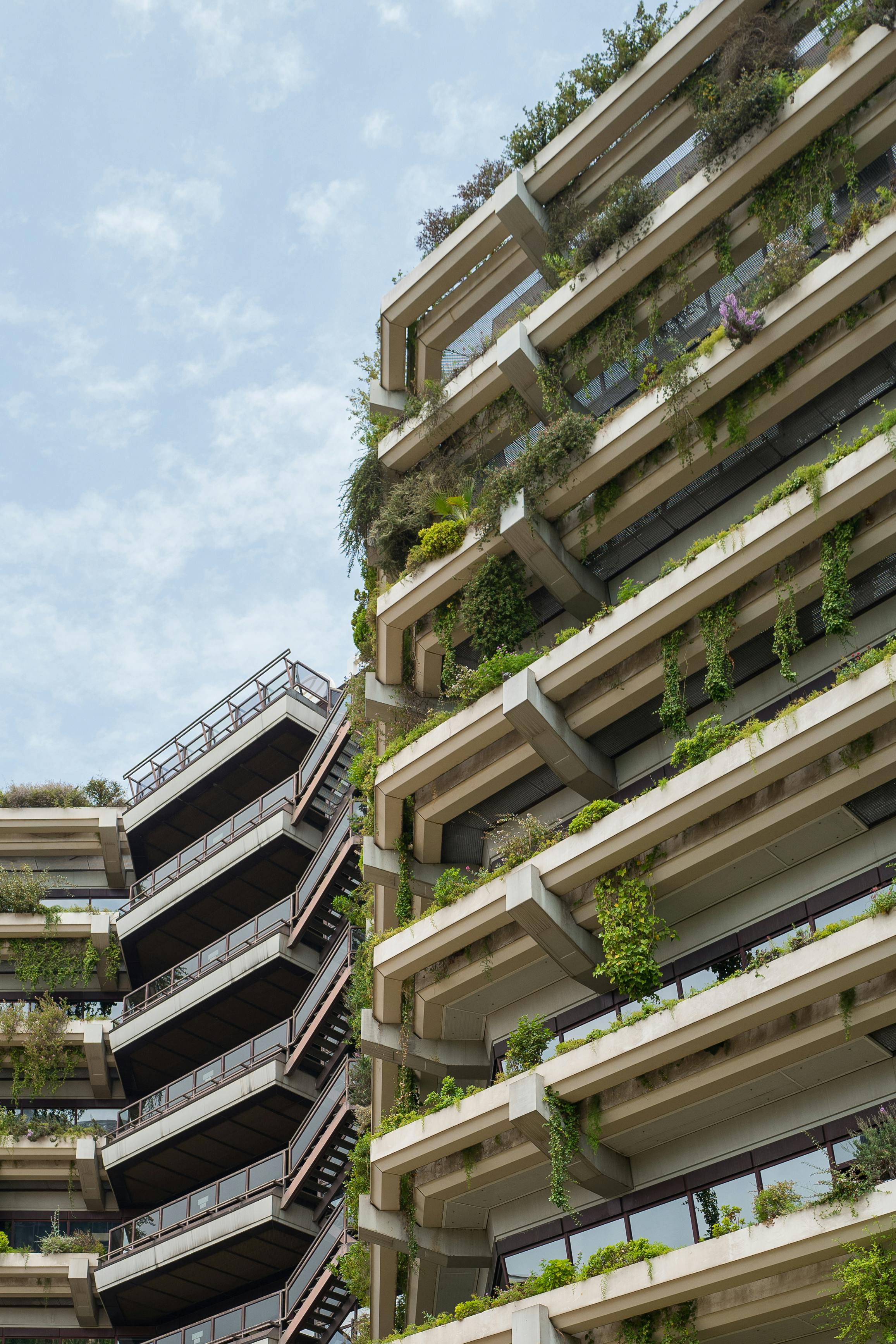 The exterior of a modern residential building in Barcelona, with concrete balconies overflowing with vibrant green plants.